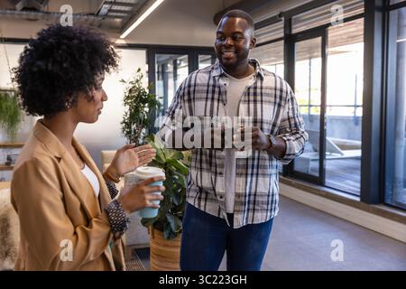 Divers collègues debout dans le salon de bureau près des fenêtres tenant une tasse à café et un gobelet réutilisable Banque D'Images