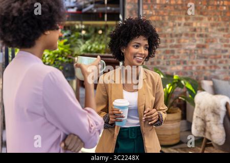 Diverses collègues féminines tenant des tasses et bavardant dans le salon de bureau avec des plantes en pot, espace de copie Banque D'Images
