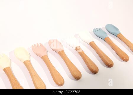 Ensemble de cuillères et fourchettes en silicone colorées pour bébé avec poignées en bois Banque D'Images