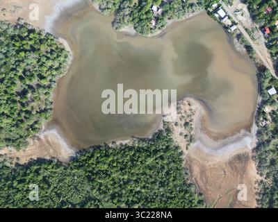 Une large perspective aérienne montre une rivière douce serpentant à travers une riche végétation verdoyante sous un ciel clair, créant un environnement paisible. Banque D'Images