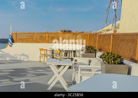 Café confortable sur Santorin près d'un moulin à vent avec clôture en bois et drapeau grec Banque D'Images