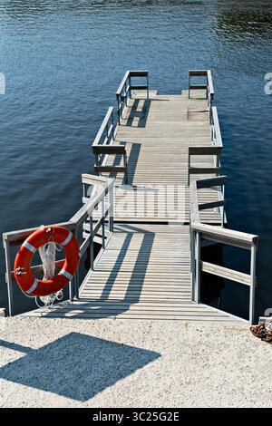 Quai en bois s'étendant au-dessus de l'eau calme avec une bouée de sauvetage dans un cadre serein au bord du lac Banque D'Images