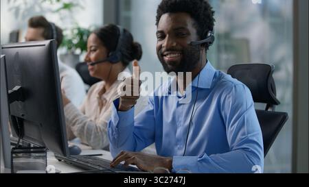 Équipe multinationale hommes africains opérateurs de centres d'appels pouce vers le haut casque souriant ordinateur de bureau soutien femme indienne dactylographiant service client Banque D'Images