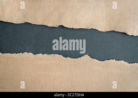 Carton brun papier déchiré bords déchirés laissant un trou horizontal au centre, sur fond gris foncé. Copier l'espace. Banque D'Images