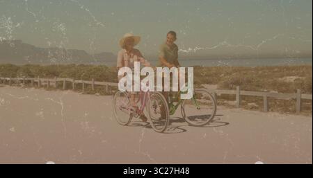 Couple d'équitation sur des croiseurs vert rose le long d'un sentier côtier pavé, chapeau de soleil à large bord, barrière de rail basse Banque D'Images