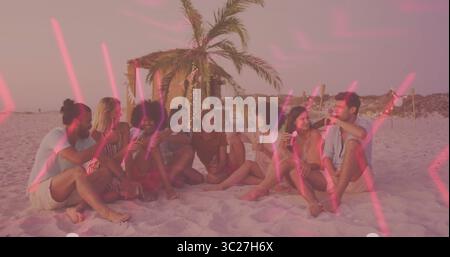 Groupe de huit amis serrant des bouteilles et des verres sur la plage au coucher du soleil, avec une cabane de palmiers éclairée Banque D'Images