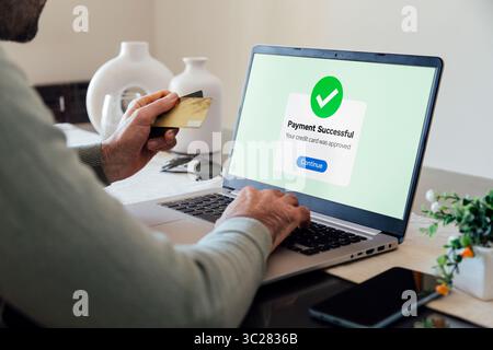Effectuer un paiement par carte de crédit ou de débit en ligne. Confirmation de paiement numérique réussie sur un écran d'ordinateur portable. Homme dans son salon complétant un achat Banque D'Images