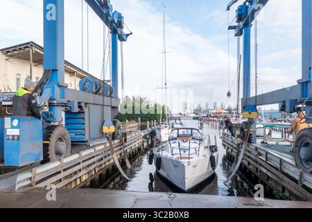 Warns, pays-Bas - 20 novembre 2023 : grue de levage de bateau préparée pour hisser un voilier hors de l'eau dans une marina animée, avec des compétences de travailleurs Banque D'Images