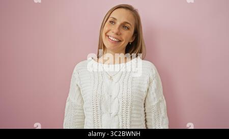 Femme souriante devant un mur rose, présentant un style de pull tricoté décontracté avec une expression agréable isolée qui respire la chaleur et positivit Banque D'Images