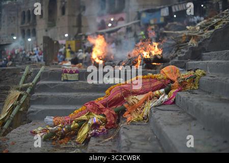11 avril 2019 : Varanasi, Inde : le corps d'un homme récemment décédé, enveloppé dans un tissu coloré et orné de soucis, est assis sur les marches de l'un des ghats brûlants de Varanasi. Quand une personne meurt, ses restes sont enveloppés dans un tissu coloré et ornés de soucis, avant d’être mis sur une civière et défilés dans les ruelles de la vieille ville de Varanasi avant de se retrouver sur les rives du Gange. Là, le corps est submergé dans les eaux saintes de la rivière, avant d'être dehors pour sécher avant d'être enfin incinéré. (Crédit image : © Tobin Jones/ZUMA Wire) Banque D'Images