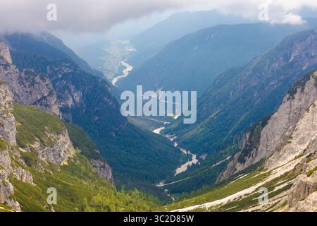 Vue panoramique sur la vallée alpine depuis Tre Cime di Lavaredo, avec rivière sinueuse, forêts luxuriantes, falaises abruptes et nuages bas suspendus. Banque D'Images