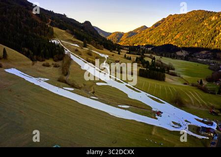Vue aérienne de neige blanche contrastant avec les champs verdoyants et les montagnes dorées, créant un paysage hivernal serein, Bad Hindelang, Bayern, Allemagne. Banque D'Images