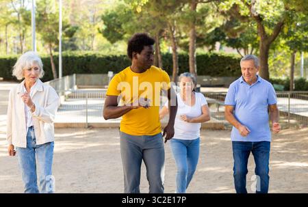 Un entraîneur afro-américain positif aidant les personnes âgées à étirer leurs muscles avant de danser à l'extérieur dans le parc Banque D'Images