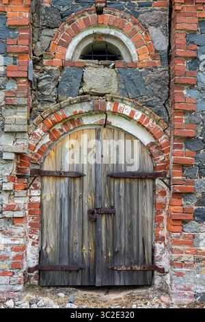 Portes en bois vieilli situées dans une façade voûtée en brique et pierre, avec une petite fenêtre voûtée au-dessus, mettant en valeur des détails architecturaux historiques Banque D'Images