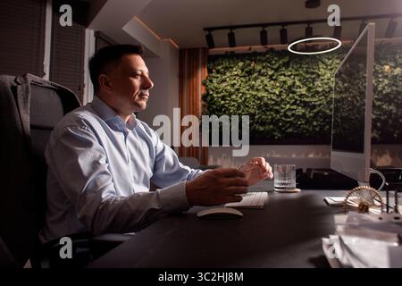 Homme d'affaires bouleversé lève les mains dans la frustration tout en travaillant à un bureau encombré. Symbole d'épuisement professionnel, de stress professionnel ou de démission. Lieu de travail. Banque D'Images