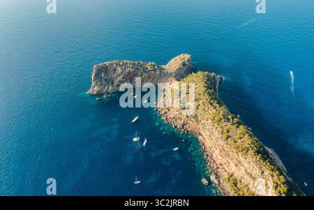 Vue aérienne d'une péninsule rocheuse rencontre la mer d'un bleu profond, voiliers parsemant les eaux turquoises, une arche naturelle encadrant l'horizon, Majorque, Espagne. Banque D'Images