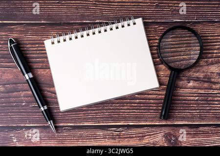 Bloc-notes vierge, loupe et stylo sur fond de bois Banque D'Images