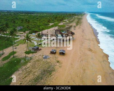 Vue aérienne de la structure altérée en bord de mer où le sable doré rencontre l'océan turquoise sous un ciel doux et couvert, Badagry, Lagos, Nigeria. Banque D'Images