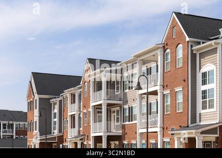 Détail d'une rangée de maisons de ville en briques et en vinyle bronzé avec des poteaux blancs sur les patios et un ciel bleu. Banque D'Images