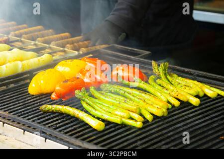 Une variété de légumes frais, y compris des tranches de poivrons et des asperges, cuisiner sur un barbecue extérieur fumé Banque D'Images