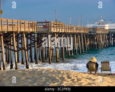 Homme se relaxant dans une chaise de plage au coucher du soleil, Balboa Pier, Newport Beach, Californie Banque D'Images