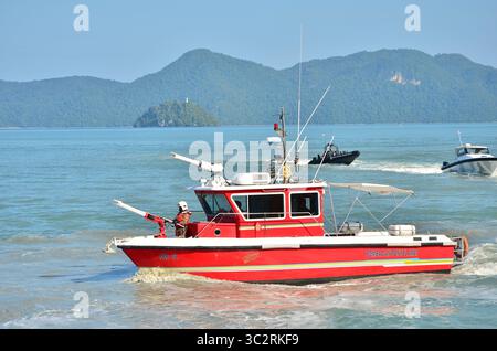 Une image d'un bateau de secours rouge menant une opération de sécurité maritime près d'îles tropicales. Banque D'Images