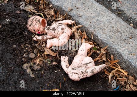 Poupée bébé cassée et sale se trouve abandonnée sur le bord de la route parmi les feuilles mortes et la boue. Une scène de délabrement urbaine envoûtante symbolisant la négligence, l'innocence perdue Banque D'Images