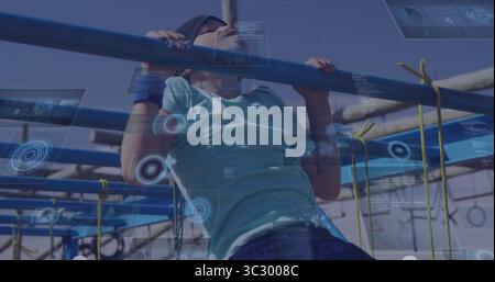 Tirant vers le haut garçon portant un bandeau et des bracelets sur des barres métalliques à la course d'obstacles, filets de corde jaune Banque D'Images