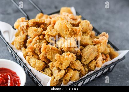 Poulet au pop-corn doré ou morceaux de poulet frit de la taille d'une bouchée, empilés haut dans un panier de service en fil noir doublé de papier blanc. Banque D'Images