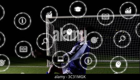 Joueur de football de plongée portant le but de sauvegarde de kit bleu sur le terrain de nuit, avec des icônes numériques Banque D'Images