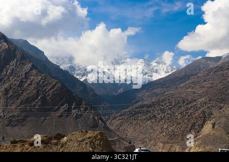 Vaste paysage himalayen avec des montagnes accidentées et arides encadrant des sommets enneigés lointains sous un ciel partiellement nuageux. Banque D'Images