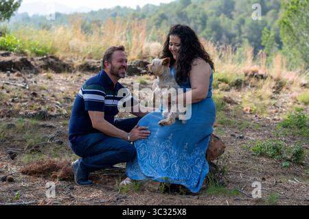 Un homme et une femme sont assis sur une bûche dans les bois avec un chien. L'homme porte une chemise rayée et un Jean. La femme porte une robe bleue. Scène i. Banque D'Images