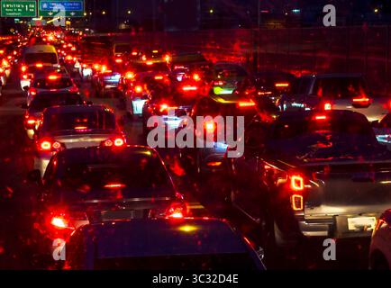 De longues rangées de voitures et d'autres véhicules font la queue, se déplaçant lentement comme beaucoup de feux de freinage rouges brillent dans l'obscurité de la nuit, sur une route principale occupée. Banque D'Images