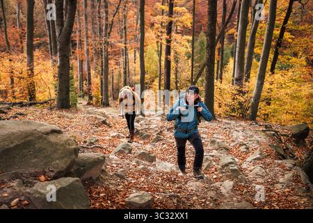 Deux randonneurs grimpent au sommet de la montagne à travers la forêt d'automne et la nature rocheuse. Randonnée en montée en terrain extrême Banque D'Images
