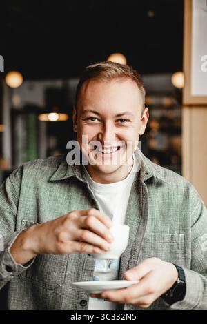 Homme souriant tenant une tasse de café dans un café confortable Banque D'Images