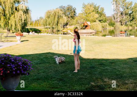 Jeune femme jouant au Frisbee avec un chien au bord du lac Banque D'Images