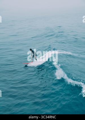 Une figure de surfeur floue solitaire perdue parmi les vagues dans un paysage marin bleu avec du mouvement Banque D'Images