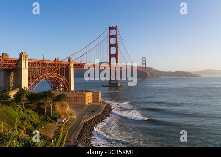 Vue imprenable sur le pont Golden Gate cuit dans la lumière chaude du soleil orange du matin, mettant en valeur la brume de l'océan et le ciel bleu profond Banque D'Images