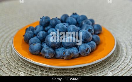 Bleuets mûrs frais dans un bol orange vif sur un napperon tissé texturé. Vue de dessus d'une collation super-alimentaire saine, riche en vitamines et antioxydants Banque D'Images