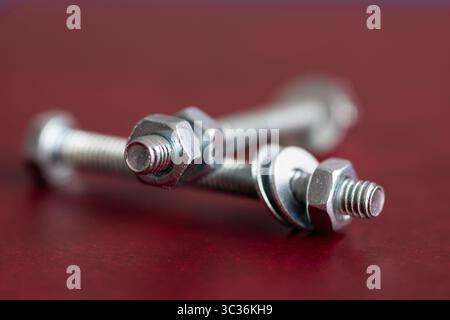 Deux boulons se superposant l'un sur l'autre sur fond rouge foncé, écrous et rondelles sont au centre Banque D'Images