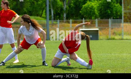 Athlètes féminines de football s'étirant par une journée ensoleillée sur un terrain herbeux Banque D'Images