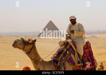 Gizeh, Egypte, 17 juillet 2025 : un touriste chevauchant un chameau devant les pyramides de Gizeh près du Caire Banque D'Images