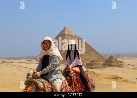 Gizeh, Egypte, 17 juillet 2025 : un touriste chevauchant un chameau devant les pyramides de Gizeh près du Caire Banque D'Images