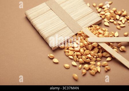 Beaux granules de cire épilatoire dorée et spatules en bois sur fond brun. Épilation, épilation, épilation indésirable. Vue de dessus Banque D'Images