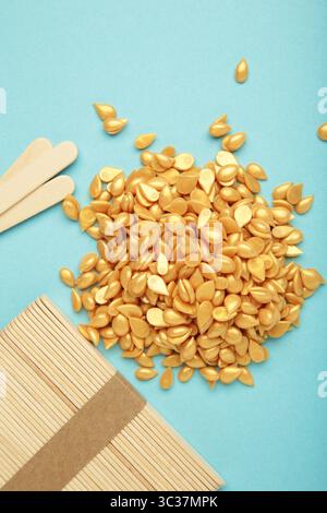 Beaux granules de cire épilatoire dorée et spatules en bois sur fond bleu. Épilation, épilation, épilation indésirable. Vue de dessus Banque D'Images