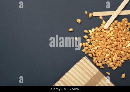 Beaux granules de cire épilatoire dorée et spatules en bois sur fond bleu foncé. Épilation, épilation, épilation indésirable. Vue de dessus Banque D'Images