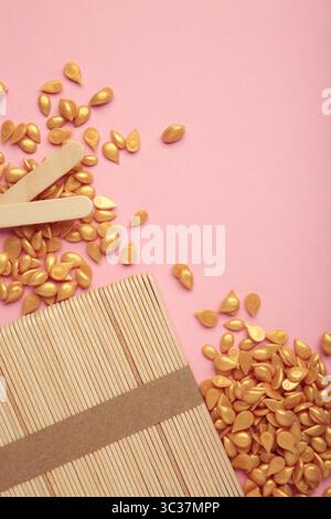 Beaux granules de cire épilatoire dorée et spatules en bois sur fond rose. Épilation, épilation, épilation indésirable. Vue de dessus Banque D'Images