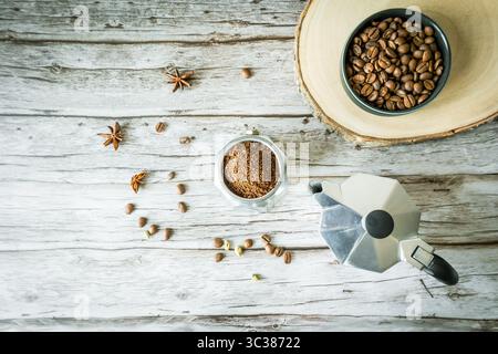 Nature morte de café rustique : arabica moulu, pot de moka et bol de haricots sur tranche de bois brut avec des épices éparpillées, ambiance de café d'automne confortable et beaucoup de copies sp Banque D'Images