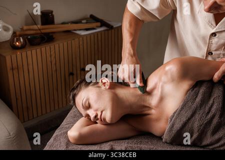 Thérapeute effectue un massage de lame gua Sha sur le cou et l'épaule pour le soulagement musculaire, la libération de tension et la relaxation profonde Banque D'Images