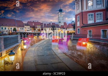 La tour historique du conseil (Turnul Sfatului) à Sibiu, en Roumanie, illuminée par la lueur chaude du coucher de soleil, avec des nuages oranges et un bleu saisissant Banque D'Images